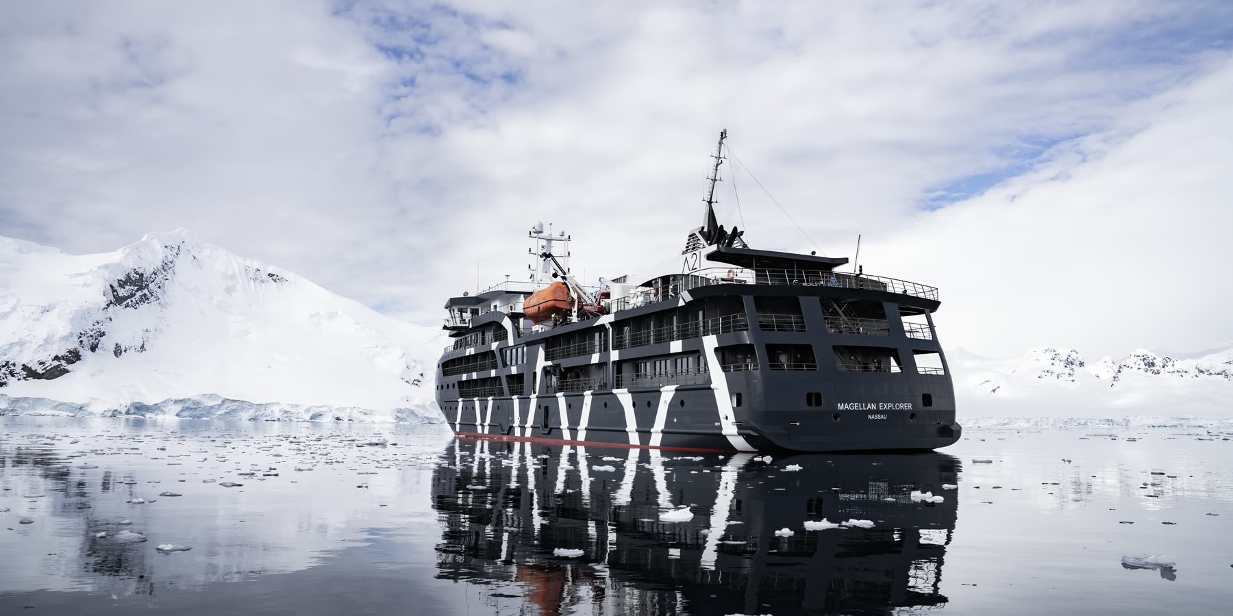Im Eis vor Anker — Magellan Explorer in stillen antarktischen Gewässern — Spiegelung vor verschneiten Bergen